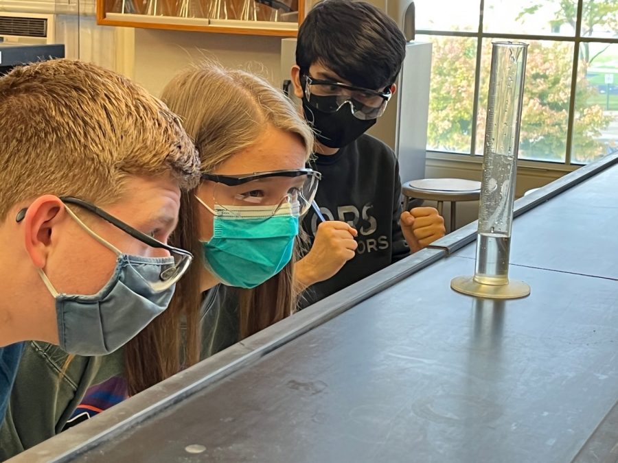 Chemistry students examine the amount of liquid in the graduated cylinder for an in-class lab. Students participate in class generated labs several times throughout the year. 