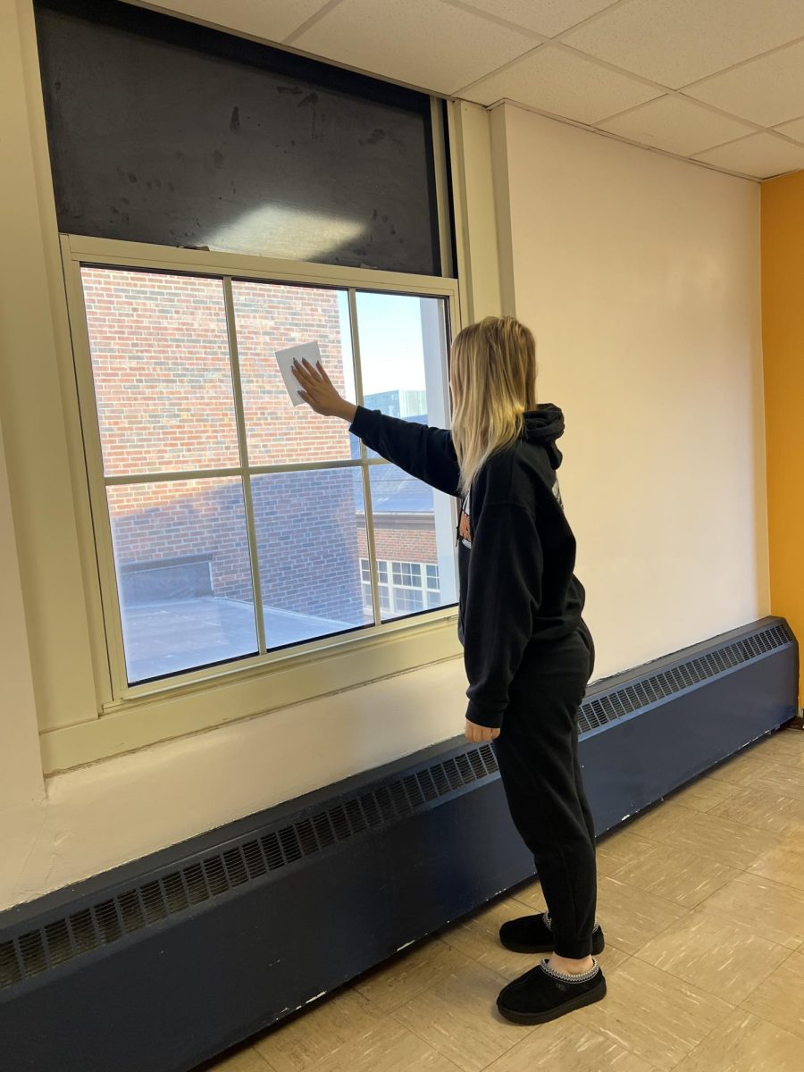 Senior Emma Sinn cleans a window with a paper towel. Students can also do this after school to reduce detention hours. 